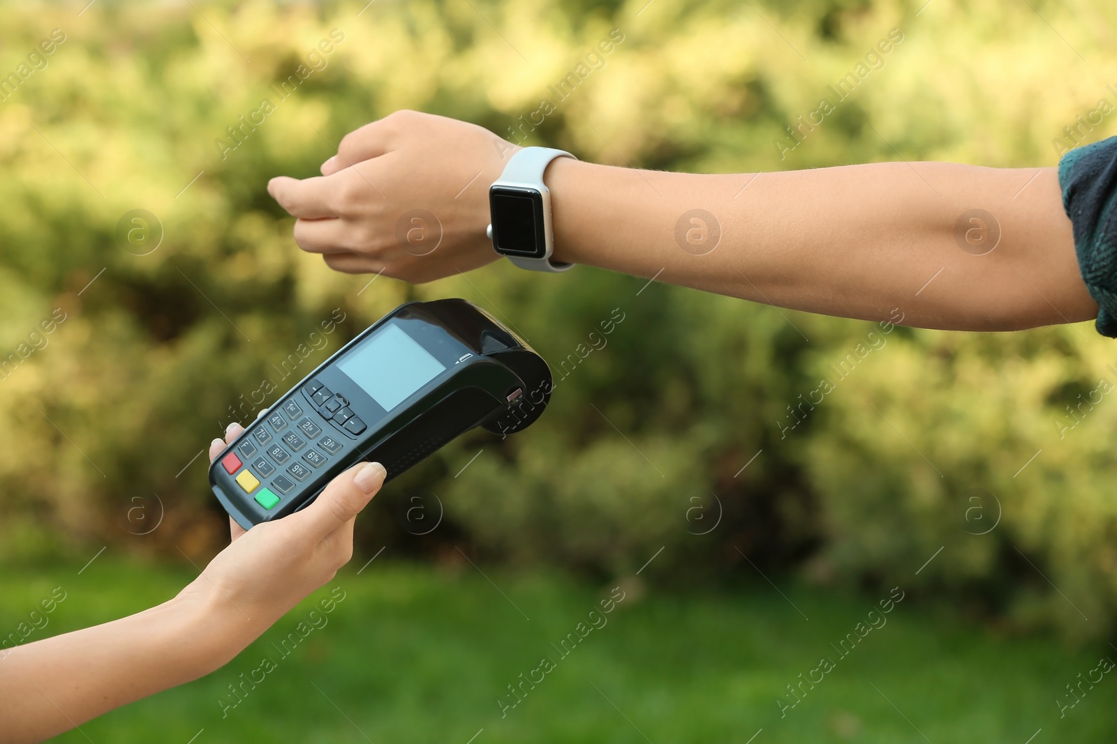 Photo of Woman using terminal for contactless payment with smart watch outdoors