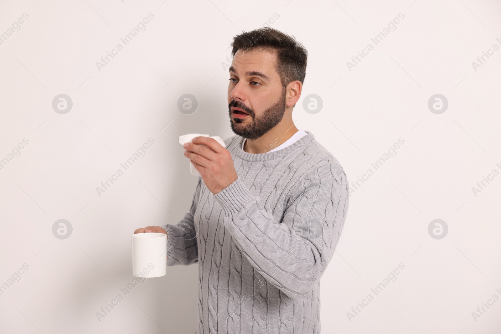 Photo of Sick man with tissue and cup of drink on light grey background. Cold symptoms