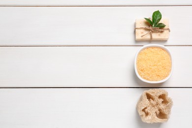 Photo of Sea salt, soap bar and loofah on white wooden table, flat lay. Space for text