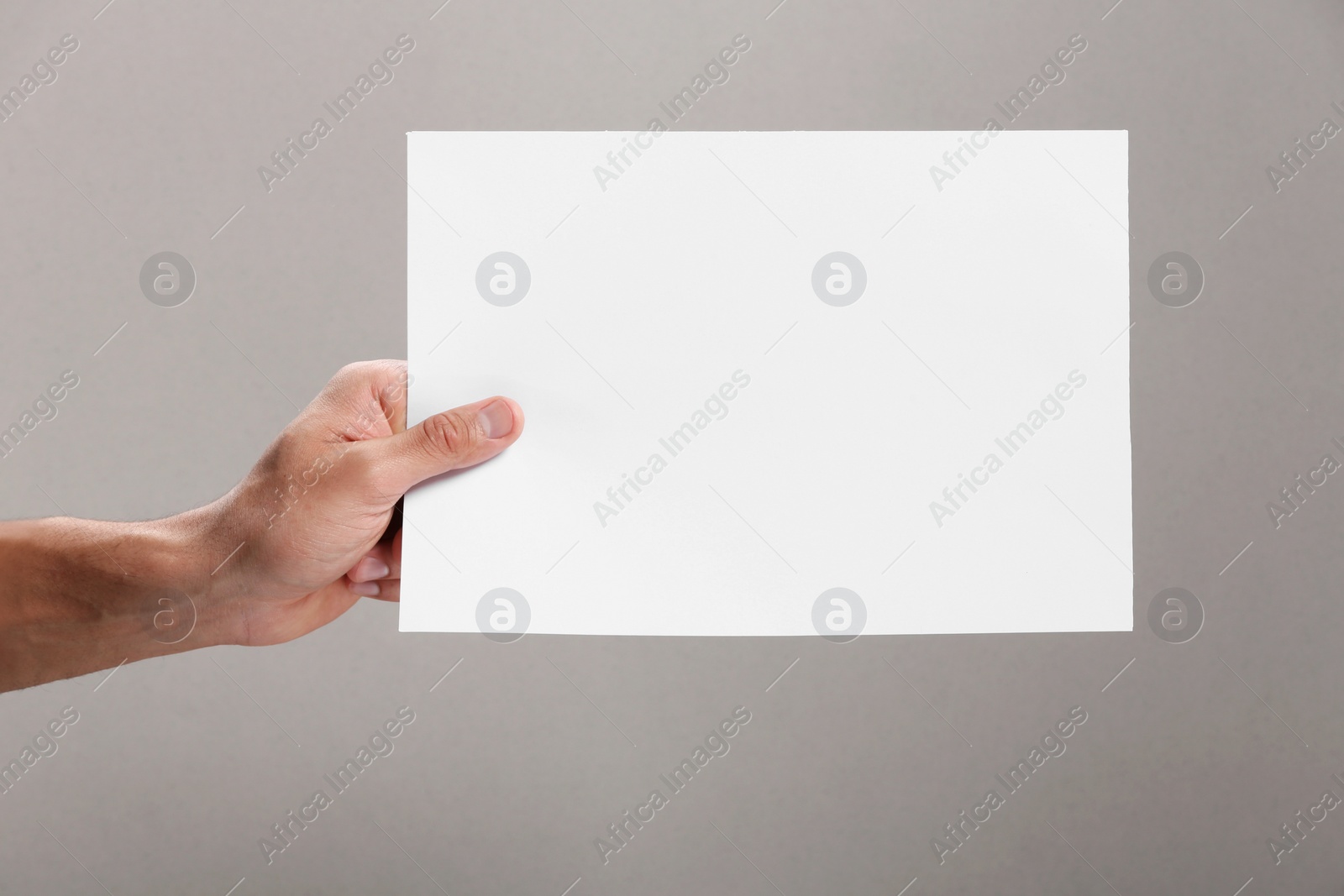 Photo of Man holding sheet of paper on grey background, closeup. Mockup for design