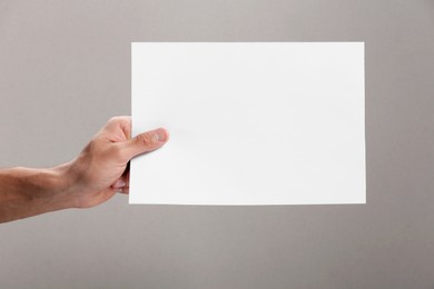 Photo of Man holding sheet of paper on grey background, closeup. Mockup for design