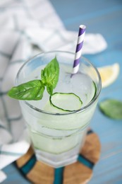 Glass of refreshing cucumber water with basil on light blue wooden table, closeup