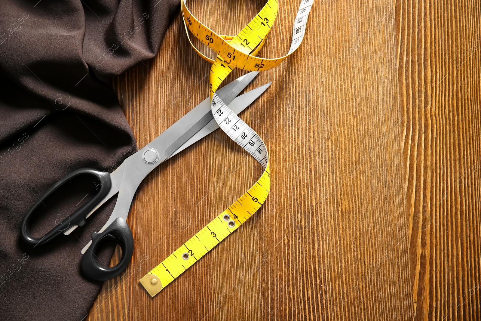 Photo of Scissors, fabric and measuring tape for tailoring on wooden background