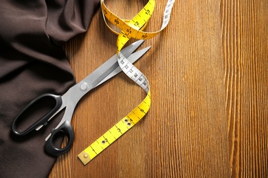 Scissors, fabric and measuring tape for tailoring on wooden background