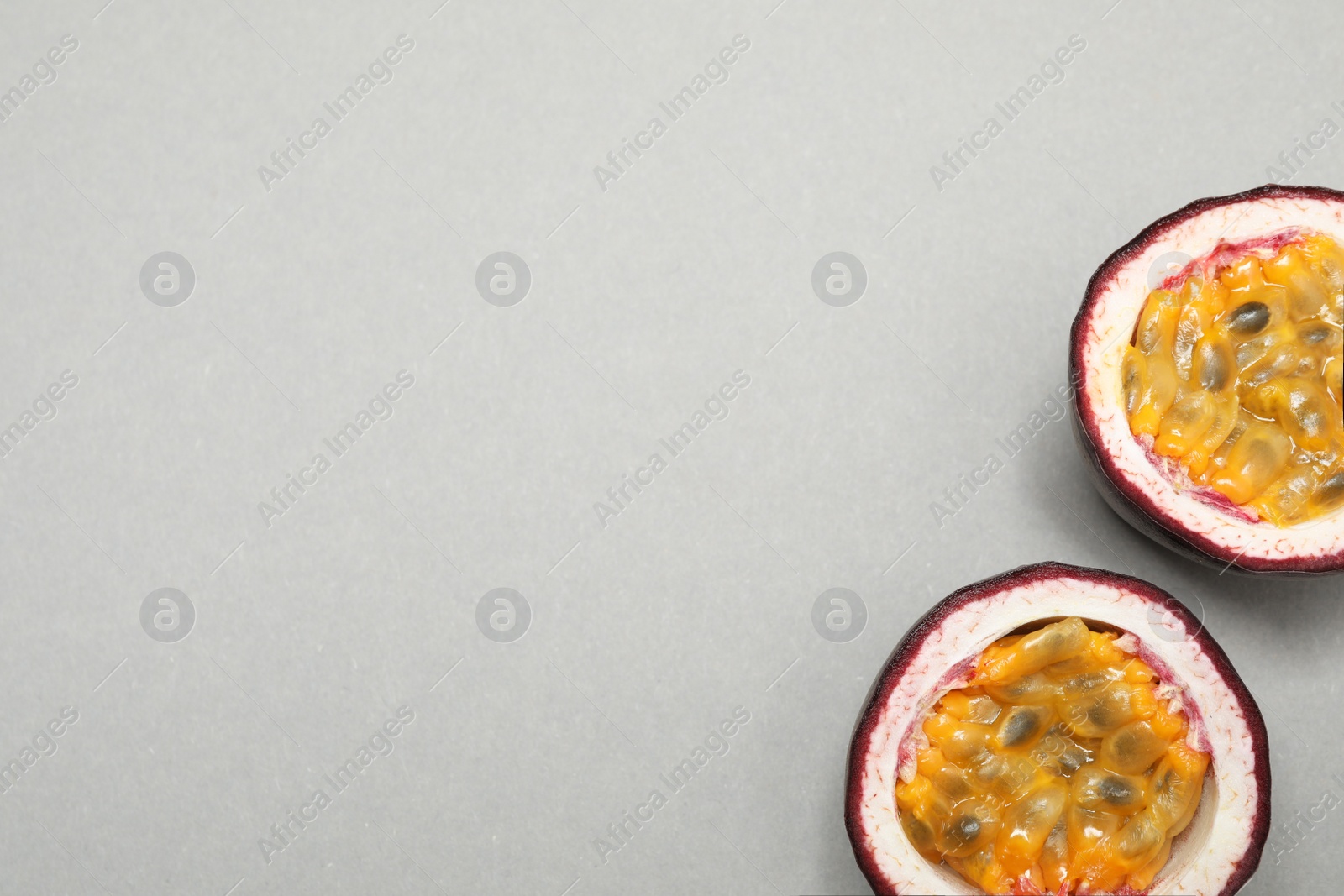 Photo of Halves of fresh ripe passion fruit (maracuya) on grey background, flat lay. Space for text