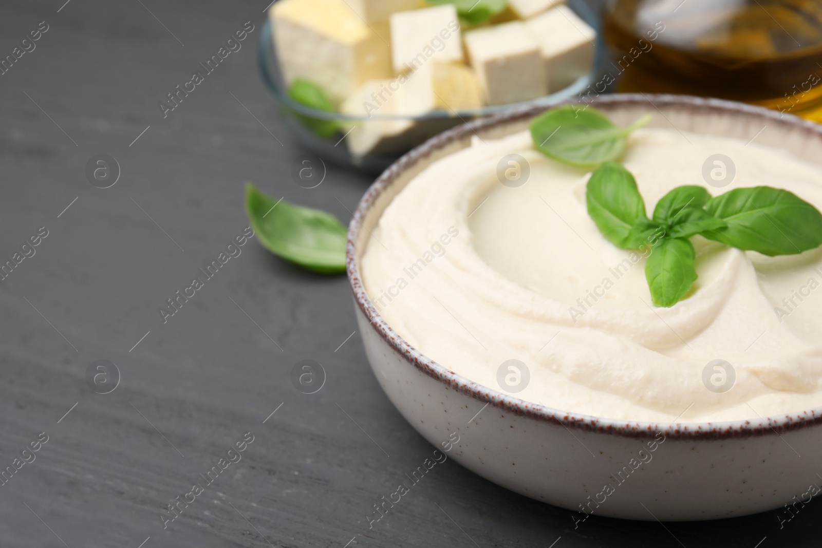 Photo of Delicious tofu sauce and basil leaves on grey wooden table, closeup. Space for text