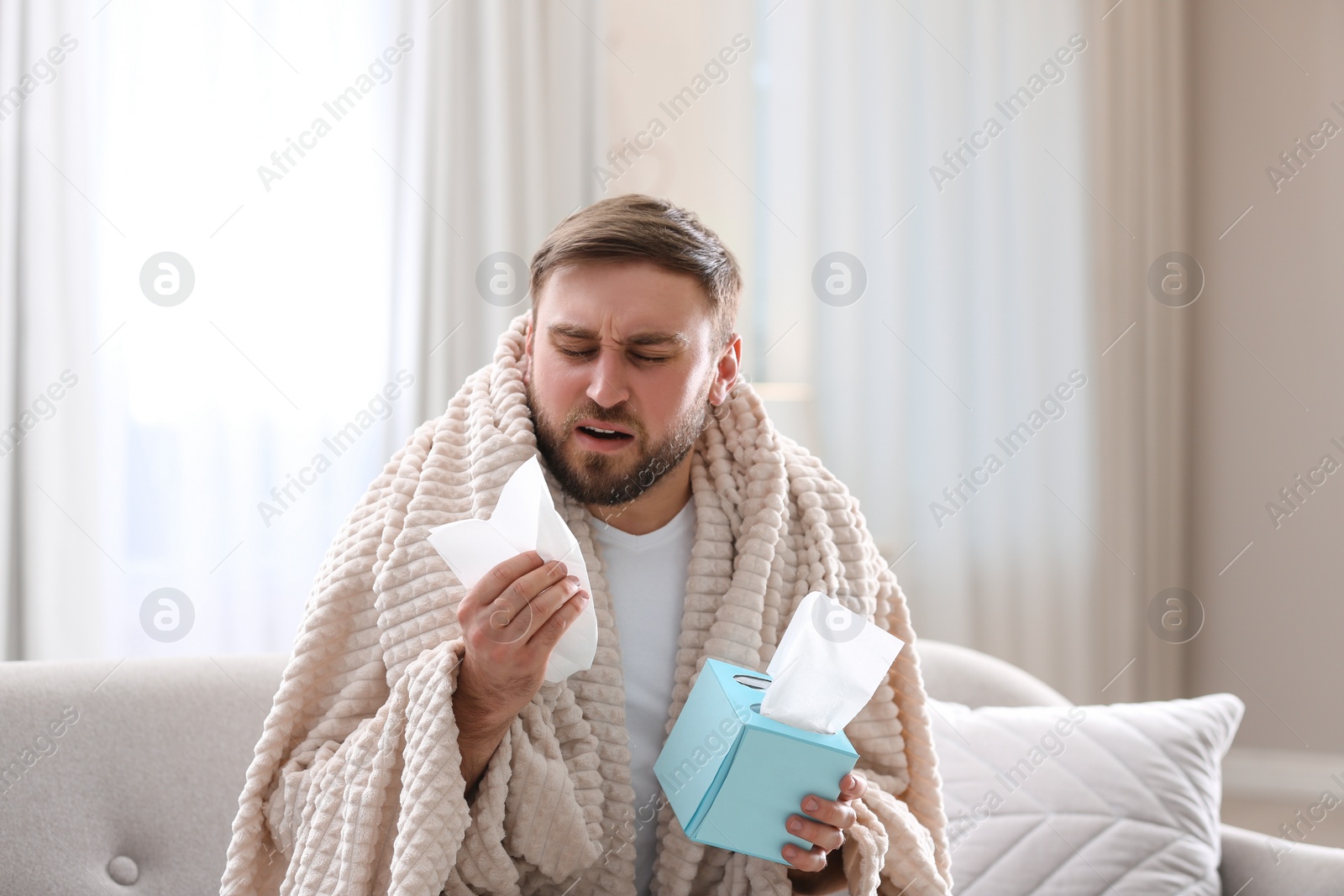 Photo of Young man suffering from runny nose in living room