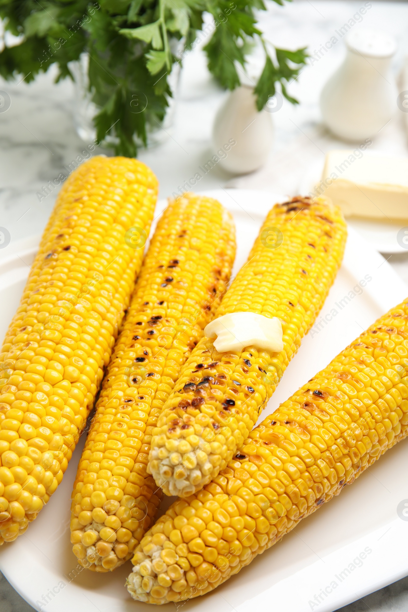 Photo of Fresh grilled corn cobs with butter on plate, closeup