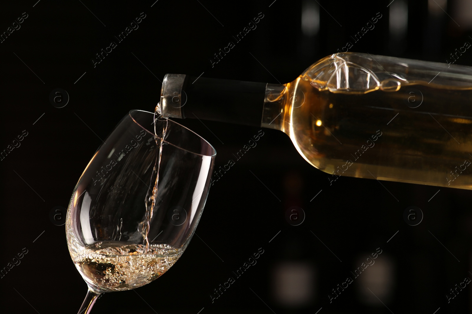 Photo of Pouring white wine from bottle into glass on blurred background, closeup