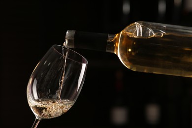 Pouring white wine from bottle into glass on blurred background, closeup