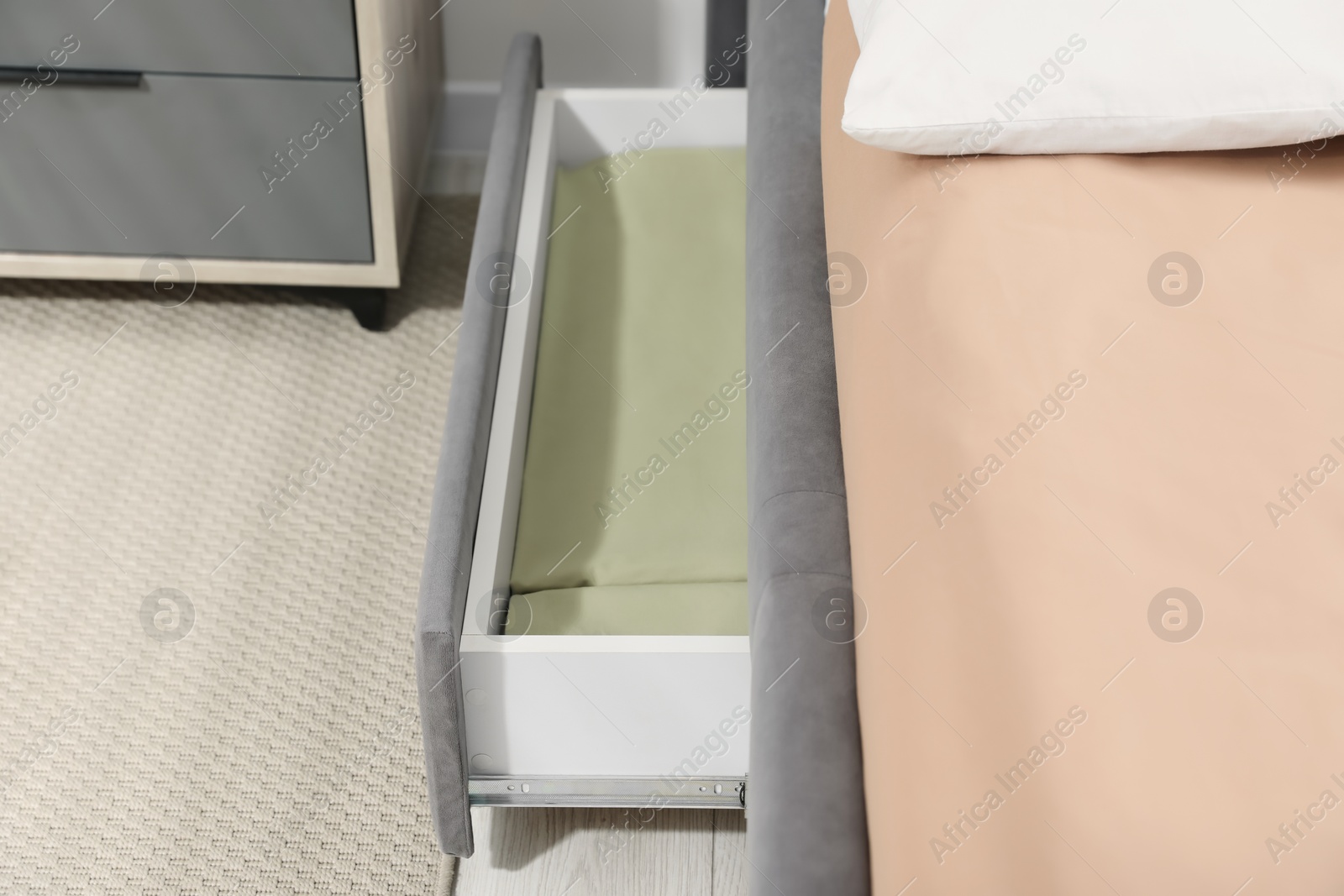 Photo of Storage drawer with bedding under modern bed in room, closeup