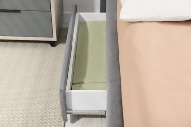 Storage drawer with bedding under modern bed in room, closeup