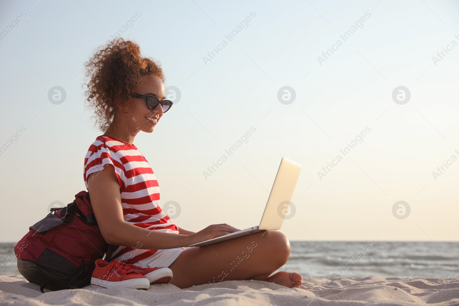 Photo of African American woman working on laptop at beach