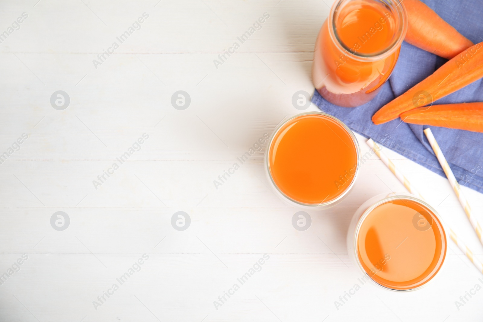 Photo of Freshly made carrot juice on white wooden table, flat lay. Space or text