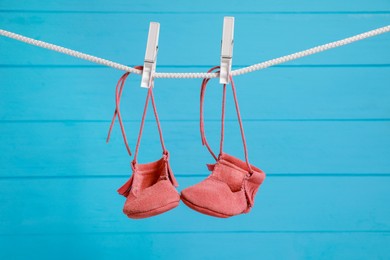 Photo of Cute baby shoes drying on washing line against light blue wooden wall