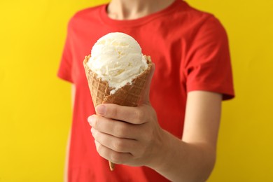 Woman holding white ice cream in wafer cone on yellow background, closeup