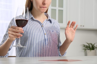 Photo of Woman with wine stain on her shirt at white marble table indoors, closeup