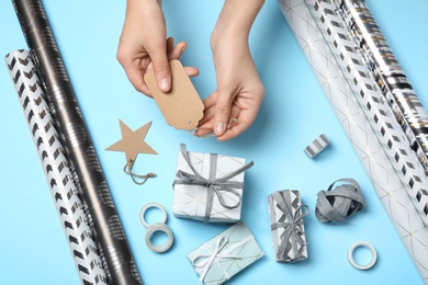 Woman attaching tag to gift box on color background, closeup