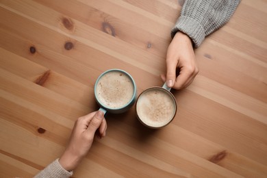 Photo of Women with cups of coffee at wooden table, top view