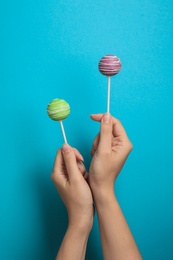 Woman holding bright delicious cake pops on color background, closeup