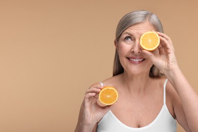Photo of Beautiful woman with halves of orange rich in vitamin C on beige background, space for text