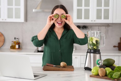 Photo of Young woman with cut kiwi for smoothie in kitchen