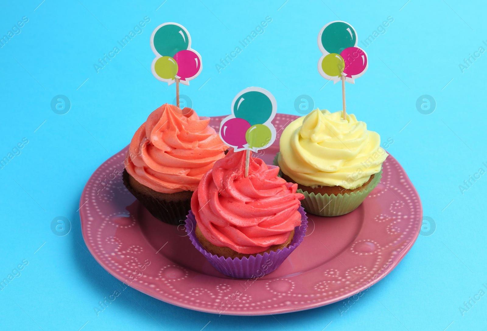 Photo of Delicious cupcakes with bright cream and toppers on light blue background