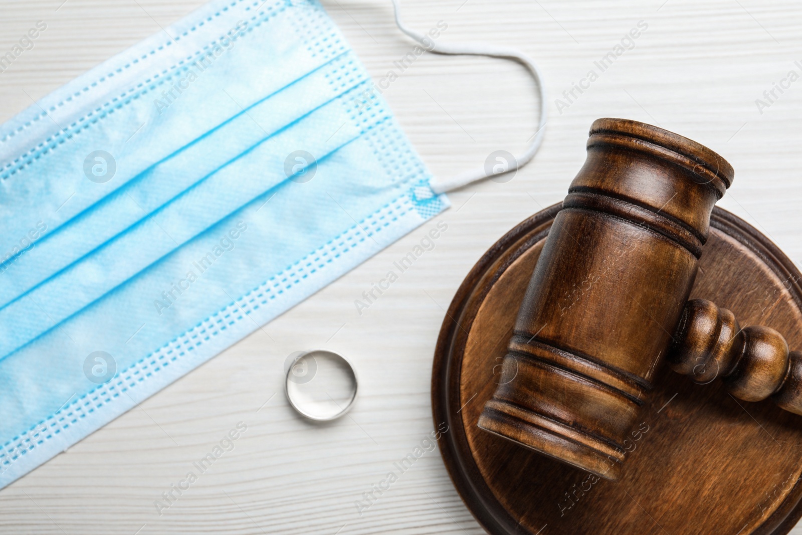 Photo of Gavel, wedding ring and protective mask on white wooden table, flat lay. Divorce during coronavirus quarantine