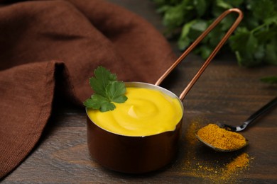 Photo of Saucepan with tasty curry sauce, powder and parsley on wooden table, closeup