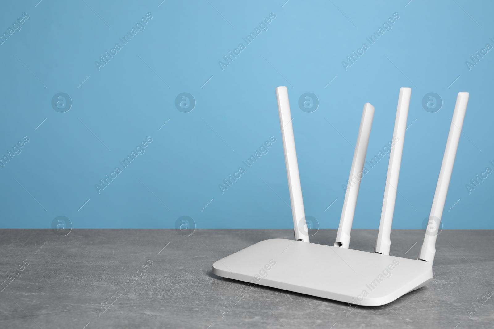 Photo of New white Wi-Fi router on grey textured table against light blue background. Space for text