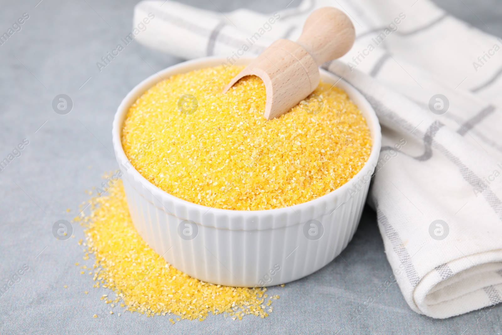 Photo of Raw cornmeal and scoop in bowl on grey table, closeup