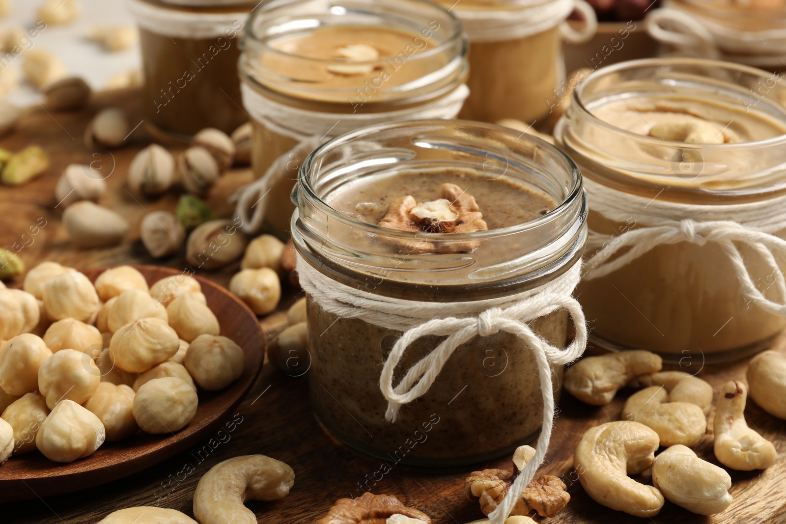 Photo of Tasty nut butters in jars and raw nuts on wooden table, closeup