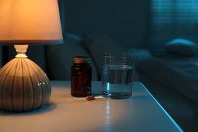 Insomnia treatment. Glass of water and pills on bedside table in bedroom at night