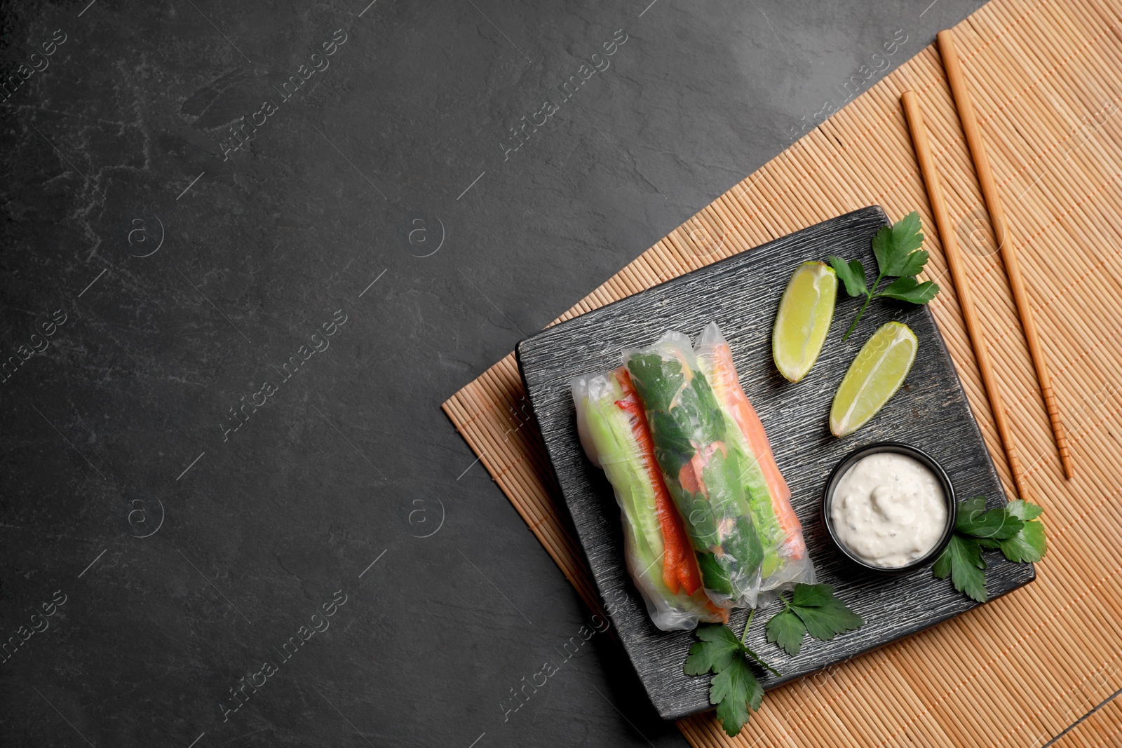 Photo of Delicious rolls wrapped in rice paper served on black table, top view. Space for text