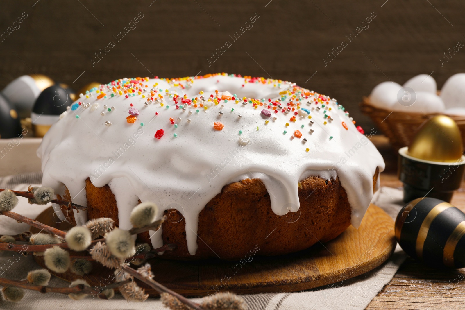 Photo of Delicious Easter cake decorated with sprinkles near eggs and willow branches on wooden table, closeup