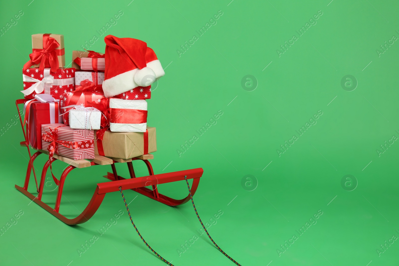 Photo of Sleigh with gift boxes and Santa's hat on green background. Space for text