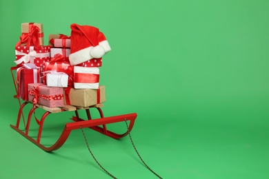 Sleigh with gift boxes and Santa's hat on green background. Space for text