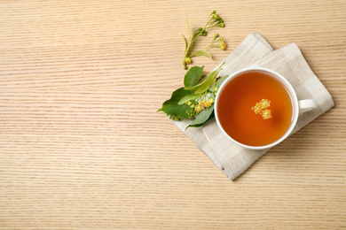 Cup of tea with linden blossom on wooden table, flat lay. Space for text