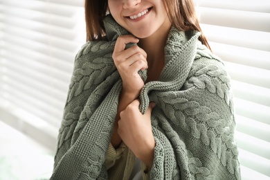 Photo of Woman covered with warm green blanket near window indoors, closeup