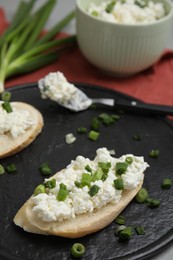 Photo of Bread with cottage cheese and green onion on slate board, closeup