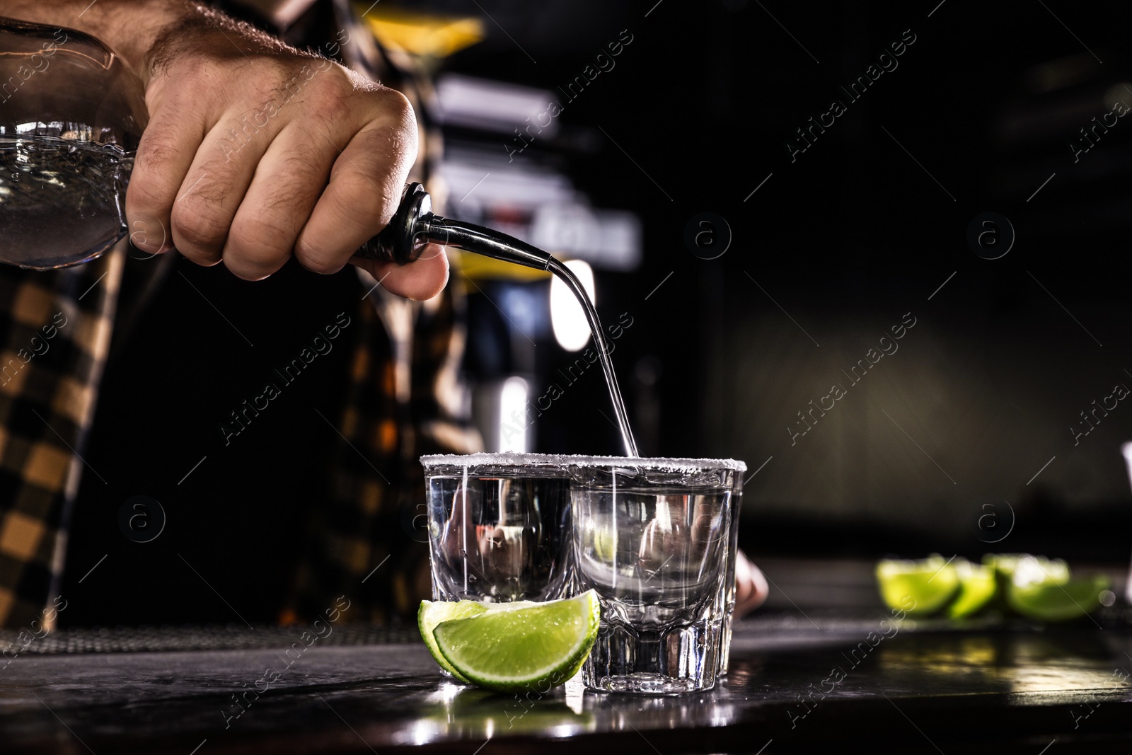 Photo of Bartender pouring Mexican Tequila into shot glasses at bar counter, closeup