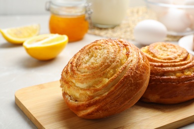 Photo of Wooden board with tasty buns on table, closeup. Fresh from oven