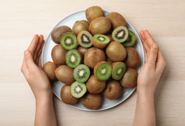 Photo of Woman holding plate with fresh ripe kiwis at light wooden table, top view