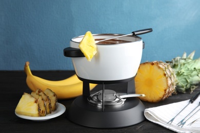 Chocolate fondue in pot and ripe fruits on wooden table