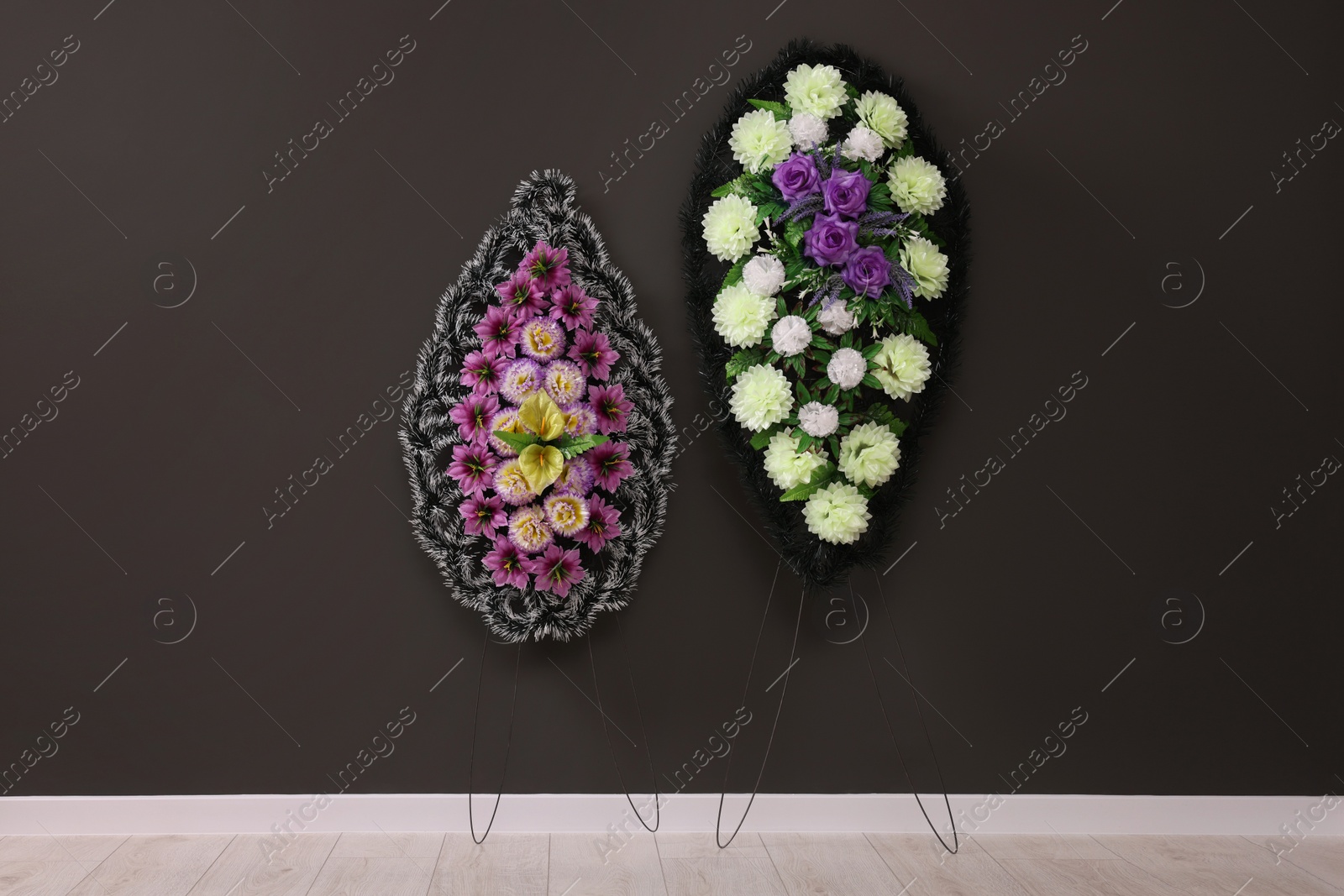 Photo of Funeral wreaths of plastic flowers hanging on dark grey wall indoors