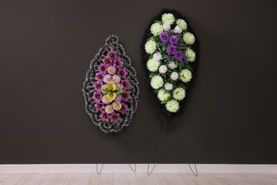 Photo of Funeral wreaths of plastic flowers hanging on dark grey wall indoors