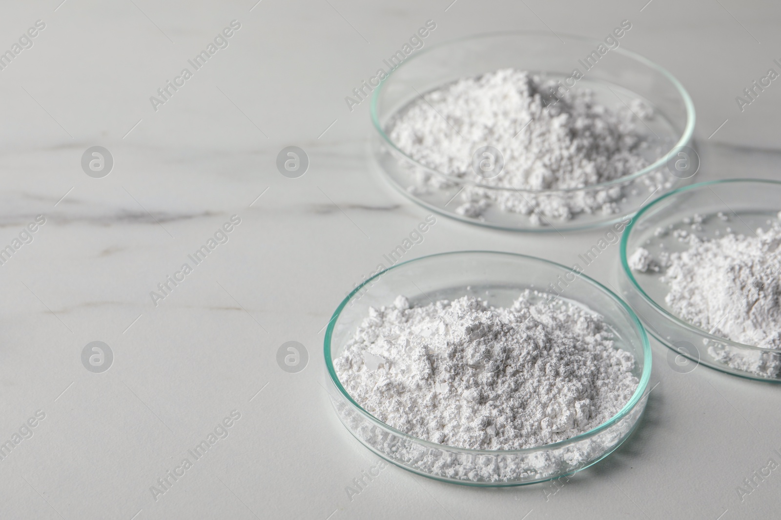 Photo of Petri dishes with calcium carbonate powder on white marble table. Space for text