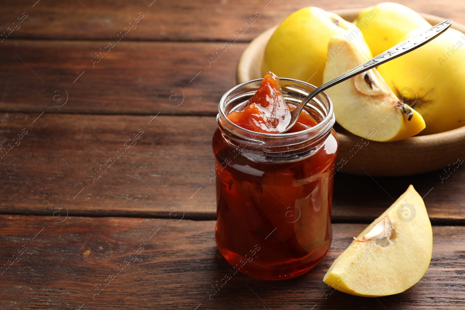 Photo of Tasty homemade quince jam in jar, spoon and fruits on wooden table. Space for text