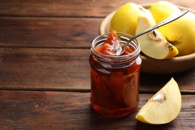 Photo of Tasty homemade quince jam in jar, spoon and fruits on wooden table. Space for text