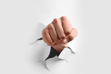Man breaking through white paper with fist, closeup